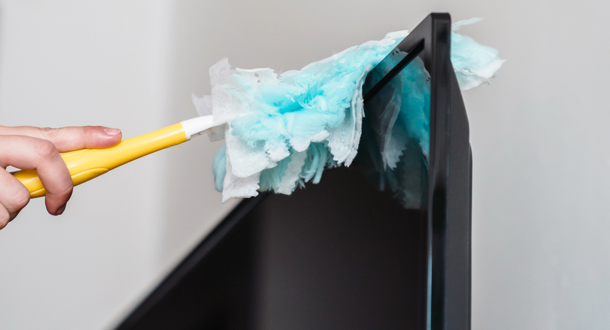 A human hand dusting a television with a duster