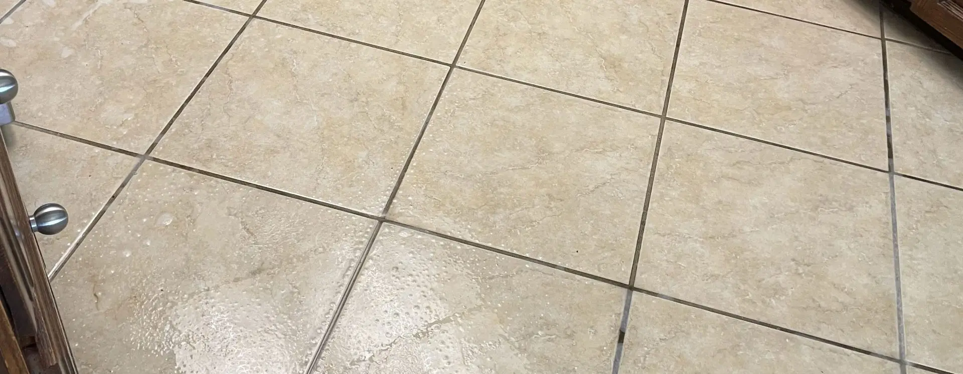 Beige ceramic tile floor with darkened grout lines before cleaning